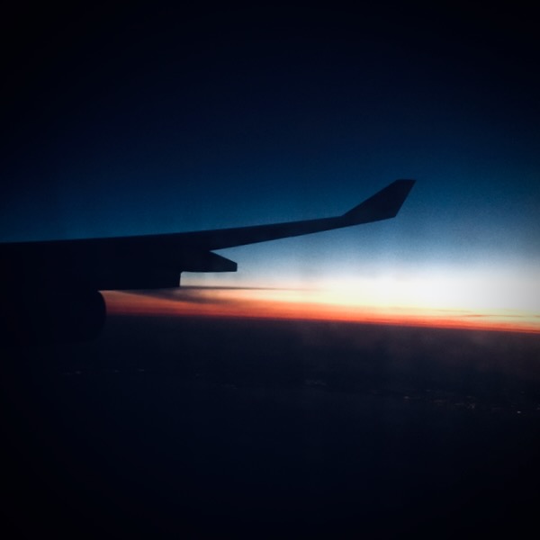 Une aile d'avion vue depuis la vitre avec un ciel bleu/noir teinté de rouge.