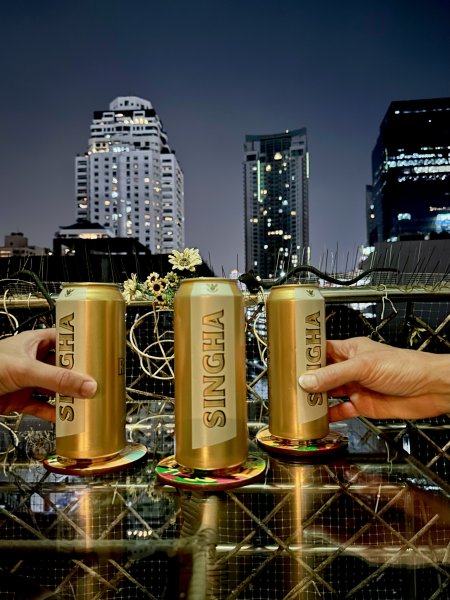 Trois bières dorées posées sur une table, deux mains, des immenses tours illuminées en arrière plan