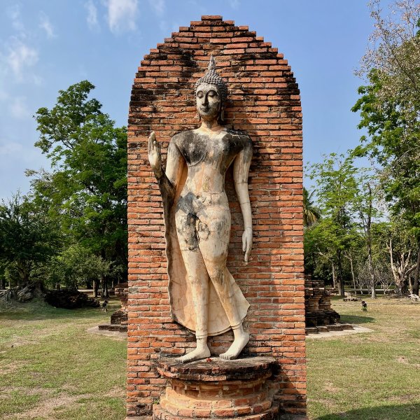 Une statue de bouddha en position de marche devant un mur de brique.