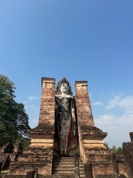 Un grand bouddha debout entre deux parois de briques.
