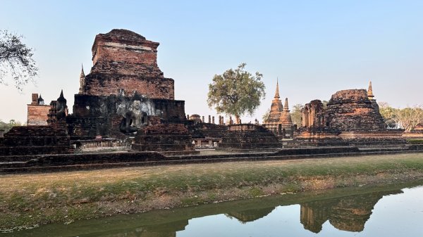 Un grand bouddha assis et des temples derrière un plan d'eau verte.