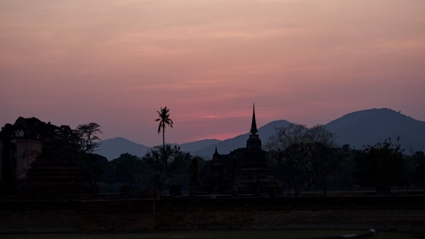 Un site archéologique avec une tour conique et pointue qui se découpe en ombre chinoise devant la montagne et le couché de soleil.