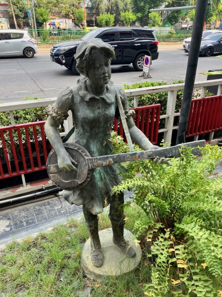 Une statue en bronze devant le bâtiment de brocante d'une jeune fille jouant du banjo.