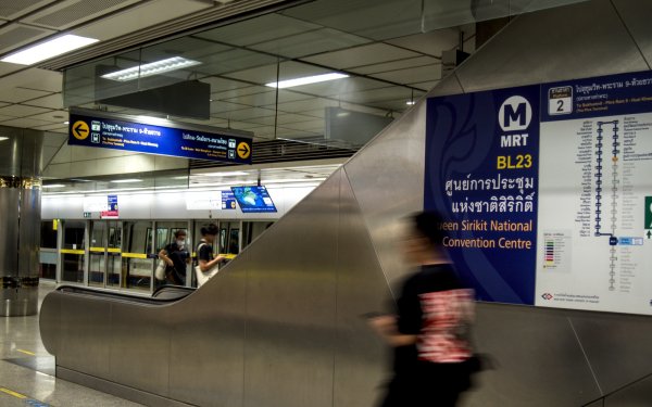 Une autre vue du métro avec des panneaux en Thaïlandais, un escalator et une silhouette floue d'homme qui marche en direction du quai.