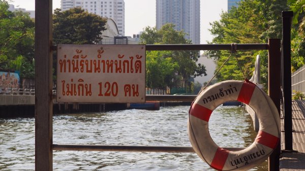 Une bouée de sauvetage accrochée sur un embarcadère du canal avec un panneau en Thaïlandais à  côté.
