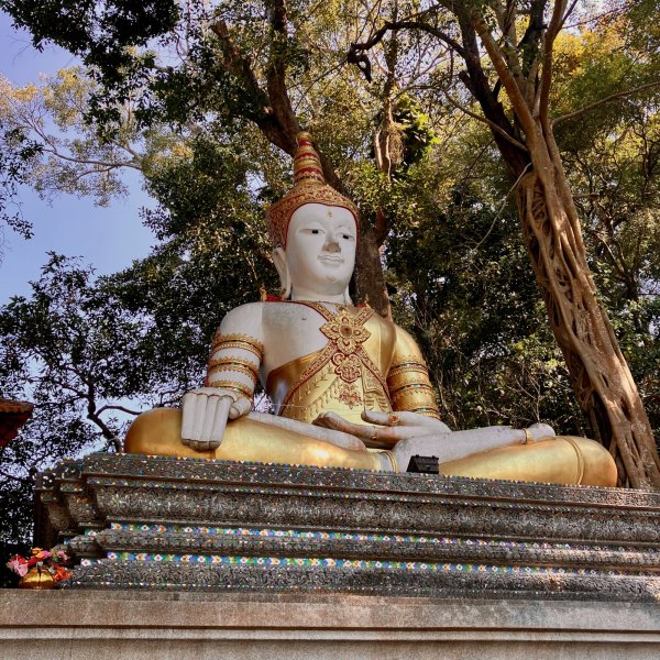 Un grand Bouddha assis en tailleur au sommet de la montagne. Il est blanc avec des dorures, l'air serein, les mains posées sur les cuisses.
