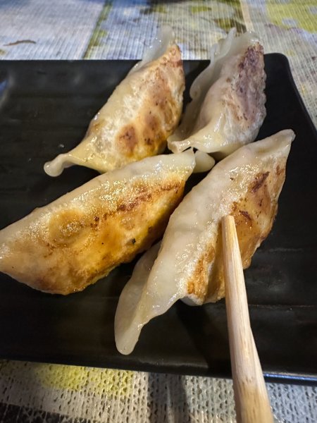 Des Gyosas dans une assiette noire avec des baguettes.
