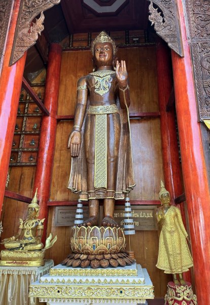 Une grande statue en bois dans une niche, un bras le long du corps, l'autre replié et la paume ouverte, signe de paix.