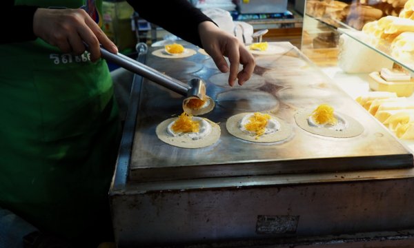Les mains d'une femme qui fait des sortes de petites crêpes roulées et farcies de lamelles orange.