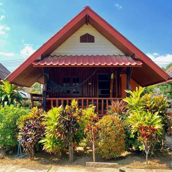 Un bungalow en bois surélevé avec une varangue devant et de la verdure autour.