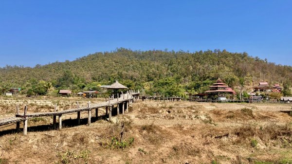 Un pont en bambou qui traverse les rizières, en arrière plan des maison avec des toits pagodes.