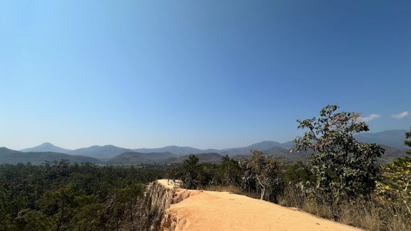 Un chemin de terre ocre clair avec vue sur les montagne en face.