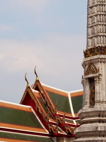 Les toits superposés du temple en brique rouge et verte surmonté de têtes de serpents, à droite une tour en pierre et des petites statues dans des niches.