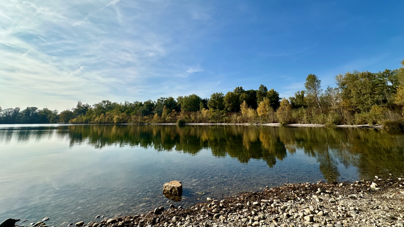 Une pierre posée sur les galets semble flotter sur l'eau. Les teintes sont plus chaudes, les arbres sur la berge, roussissent.